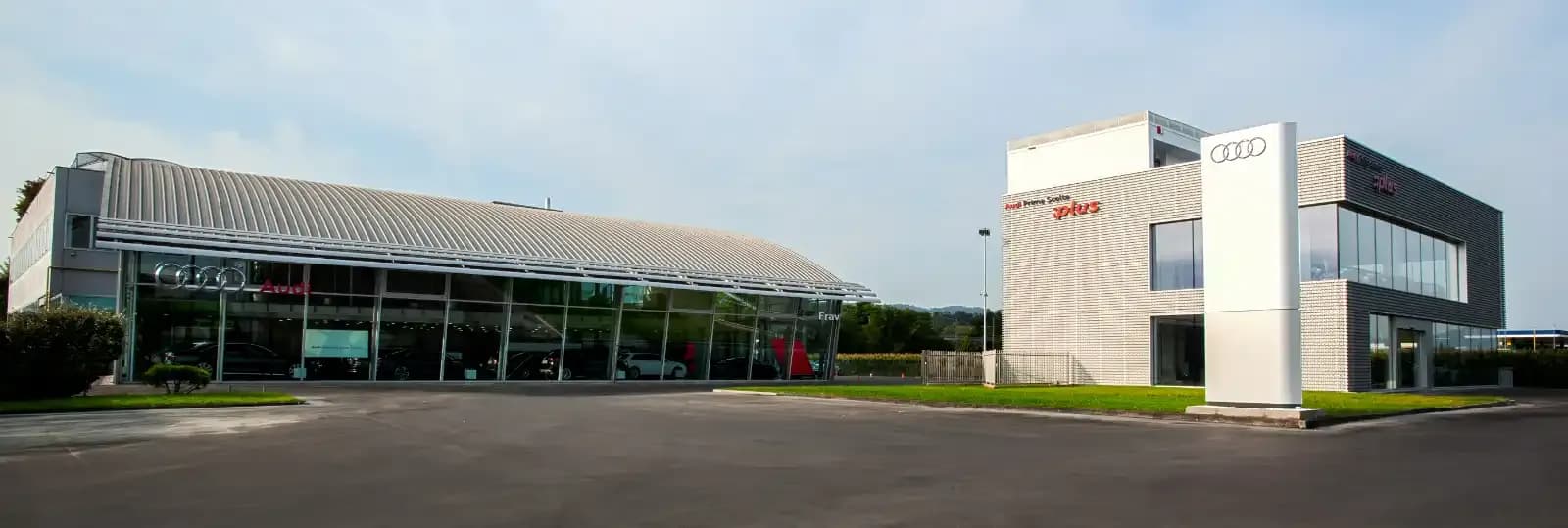 Sede Audi Frav ad Altavilla Vicentina: showroom con tetto curvo in metallo e vetrate, accanto a un edificio con logo Audi su totem bianco