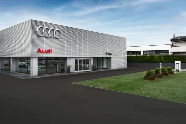 Filiale Audi Frav a Zanè: edificio con facciata a griglia metallica chiara, logo Audi e insegna Frav, con prato e aiuole in primo piano