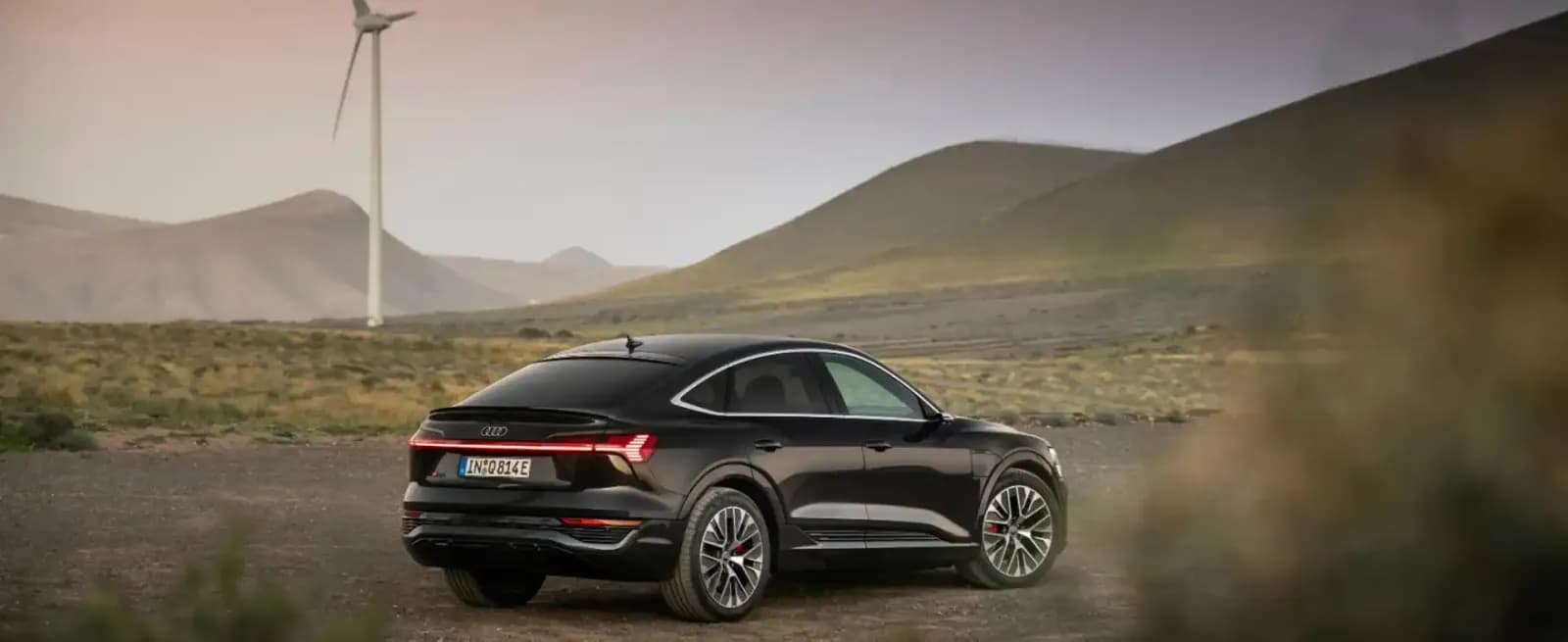 Audi Sportback elettrica nera vista di tre quarti posteriore in un paesaggio collinare, con una pala eolica sullo sfondo
