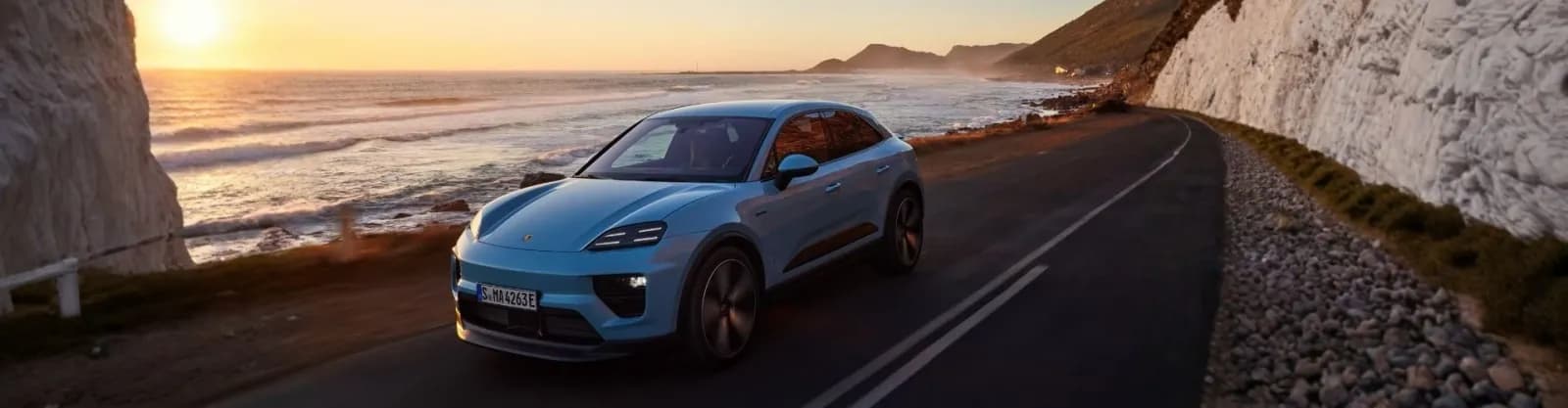 Porsche Macan elettrica azzurra su una strada costiera al tramonto