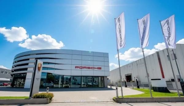 Showroom Porsche Frav ad Altavilla Vicentina: edificio con facciata curva in alluminio, insegna Porsche e tre bandiere con il marchio, sotto un cielo azzurro